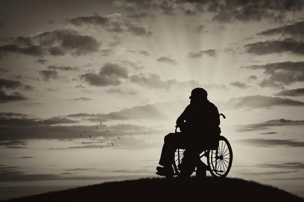 Concetto di disabilità e vecchiaia. Sagoma di persona disabile in sedia a rotelle sullo sfondo del tramonto