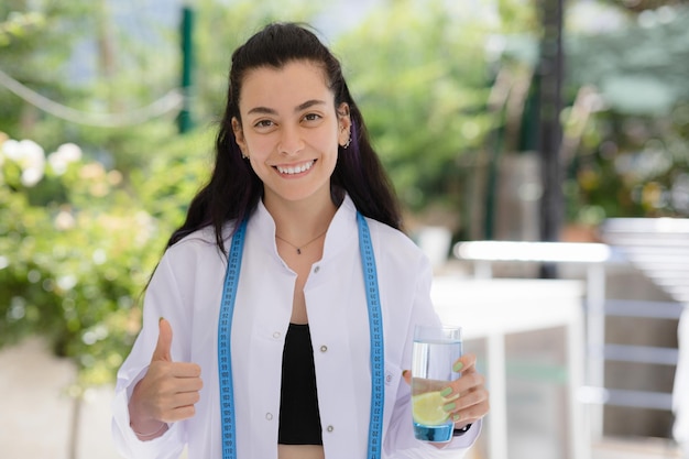 Concetto di disintossicazione Medico dietista che tiene un bicchiere d'acqua con limone e mostra il pollice in su