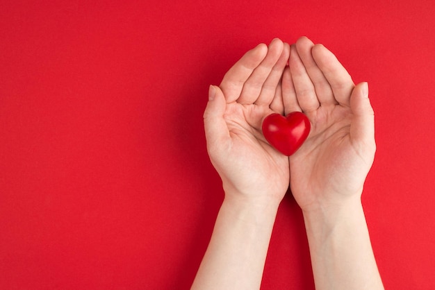 concetto di donazione. In alto sopra la foto vista dall'alto delle mani femminili che tengono il cuore rosso isolato su sfondo rosso con copyspace