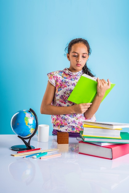 Concetto di educazione a casa - Piccola ragazza indiana o asiatica carina che studia a casa con una pila di libri, globo educativo ecc. Messa a fuoco selettiva