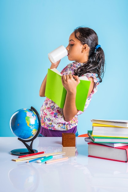 Concetto di educazione a casa - Piccola ragazza indiana o asiatica carina che studia a casa con una pila di libri, globo educativo ecc. Messa a fuoco selettiva