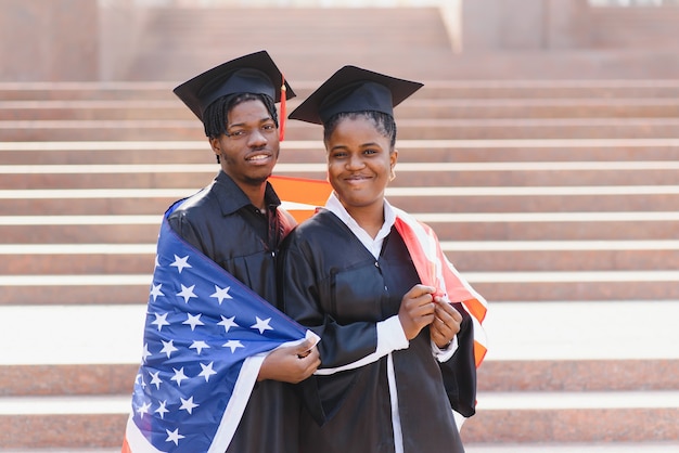 Concetto di educazione, laurea e persone - studenti internazionali felici in tavole di mortaio e abiti da scapolo con bandiera americana