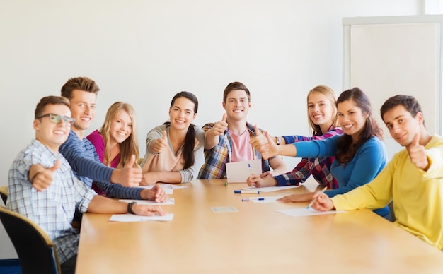 concetto di educazione, lavoro di squadra, gesto e persone - studenti sorridenti con documenti che mostrano i pollici in su e seduti al tavolo