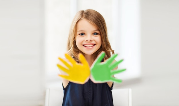 concetto di educazione, scuola, arte e felicità - piccola studentessa che mostra le mani in giallo e verde a scuola