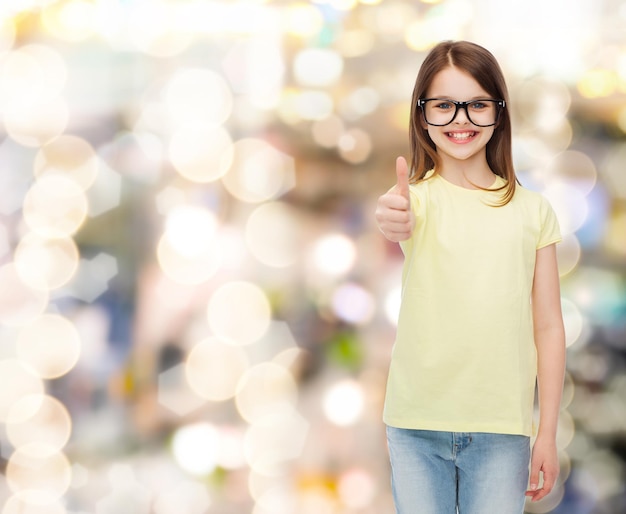 concetto di educazione, scuola e visione - bambina carina sorridente in occhiali neri che mostra i pollici in su