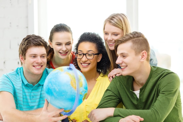 concetto di educazione, viaggi e geografia - cinque studenti sorridenti guardando il globo terrestre a scuola