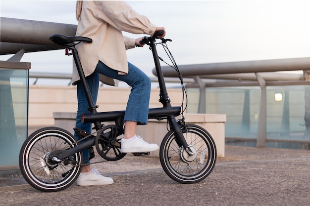 Concetto di emissioni zero Gambe di donna tagliate in sella a una bicicletta elettrica in giro per la città indossando un abbigliamento casual