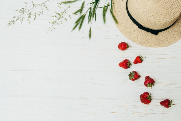 Concetto di estate, cappello di paglia, fragole fresche e steli di erba su un fondo di legno