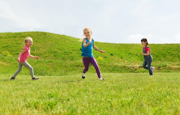 concetto di estate, infanzia, tempo libero e persone - gruppo di bambini felici che giocano a tag game e corrono sul campo verde all'aperto