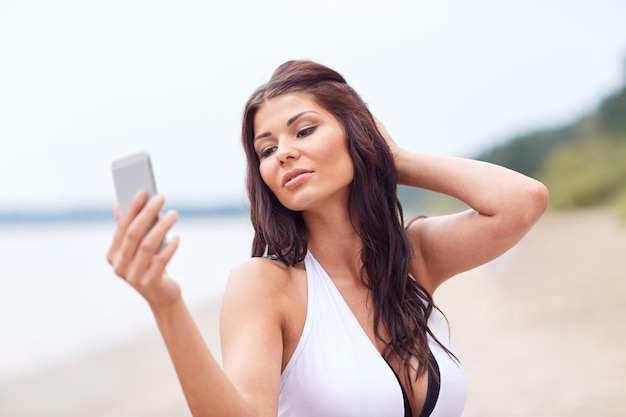 concetto di estate, viaggi, tecnologia e persone - giovane donna sexy che prende selfie con lo smartphone sulla spiaggia