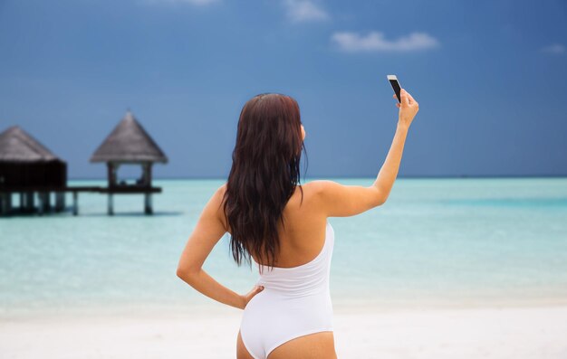 concetto di estate, viaggio, tecnologia e persone - giovane donna sexy che prende selfie con lo smartphone sopra il bungalow sullo sfondo della spiaggia