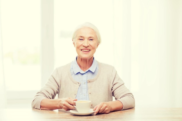 concetto di età, bevanda e persone - donna anziana sorridente felice con una tazza di caffè a casa