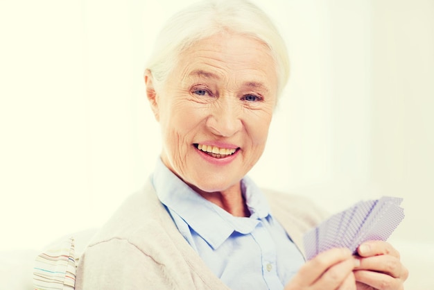 concetto di età, gioco, gioco d'azzardo, poker e persone - donna anziana sorridente felice che gioca a carte a casa