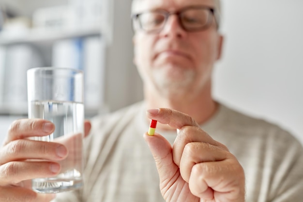 concetto di età, medicina, assistenza sanitaria e persone - primo piano delle mani dell'uomo anziano con pillola e bicchiere d'acqua a casa