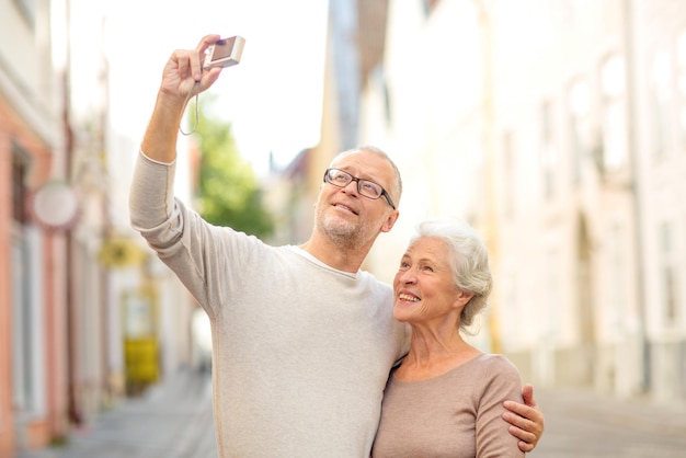 concetto di età, turismo, viaggi, tecnologia e persone - coppia senior con fotocamera che scatta selfie in strada