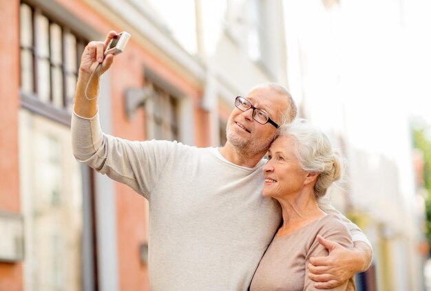 concetto di età, turismo, viaggi, tecnologia e persone - coppia senior con fotocamera che scatta selfie in strada