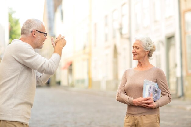 concetto di età, turismo, viaggi, tecnologia e persone - coppia senior con mappa e fotocamera che fotografano su strada