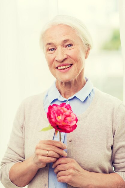 concetto di età, vacanze e persone - donna senior sorridente felice con fiore a casa