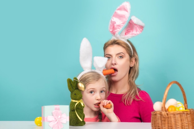 Concetto di famiglia amorevole Madre felice con sua figlia con orecchie da coniglio si stanno preparando per la Pasqua Divertenti conigliette che mangiano carote