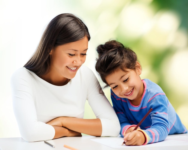 concetto di famiglia, bambini, creatività e persone felici - felice madre e figlia che disegnano con le matite su sfondo verde