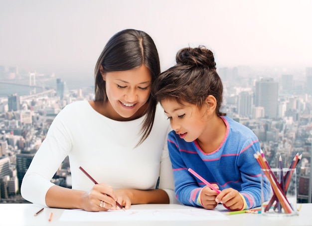 concetto di famiglia, bambini, creatività e persone felici - felice madre e figlia che disegnano con le matite sullo sfondo della città