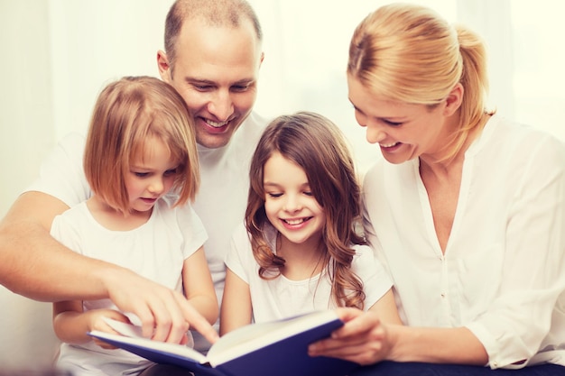 concetto di famiglia, bambini e casa - famiglia sorridente e due bambine con il libro a casa