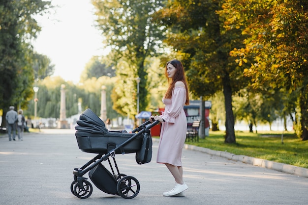 Concetto di famiglia, bambino e genitorialità - madre felice che cammina con il passeggino nel parco.