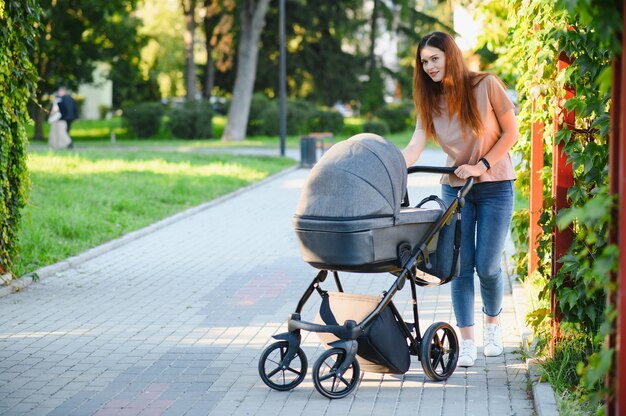 Concetto di famiglia, bambino e genitorialità - madre felice che cammina con il passeggino nel parco.