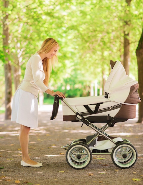 concetto di famiglia, bambino e genitorialità - madre felice con passeggino nel parco