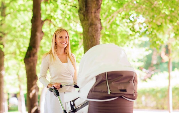 concetto di famiglia, bambino e genitorialità - madre felice con passeggino nel parco