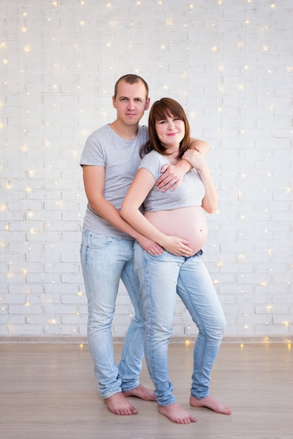 Concetto di famiglia e genitorialità coppia incinta su un muro di mattoni con luci di Natale