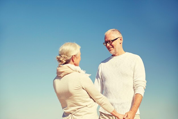 concetto di famiglia, età e persone - coppia di anziani felici che si tengono per mano e parlano all'aperto