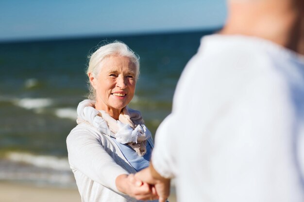 concetto di famiglia, età, viaggi, turismo e persone - coppia senior felice che si tiene per mano sulla spiaggia estiva