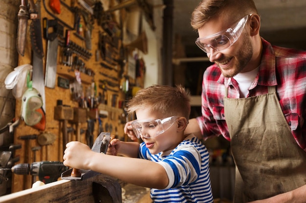 concetto di famiglia, falegnameria, falegnameria e persone - padre e figlio piccolo con aereo che lavora con tavola di legno in officina