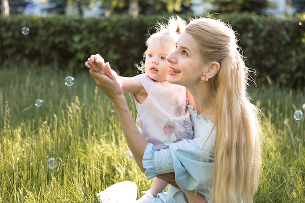 Concetto di famiglia felice con la giovane madre che gioca con la sua bambina e fa la bolla di sapone