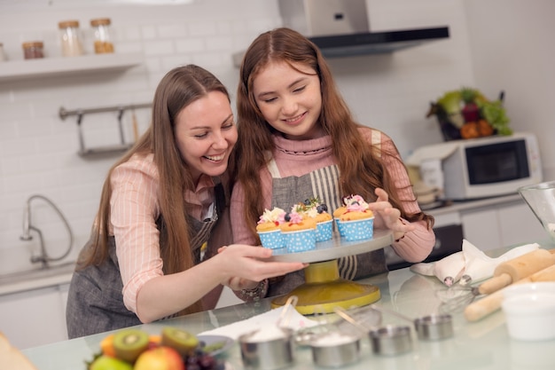 Concetto di famiglia felice di una madre e sua figlia che si godono i cupcakes insieme in cucina a casa.