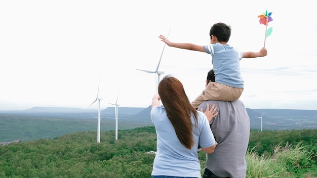 Concetto di famiglia felice e progressista che si gode il tempo trascorso presso il parco eolico Generatore elettrico dal vento tramite generatore eolico in campagna con colline e montagne all'orizzonte
