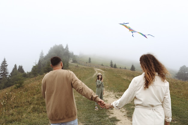 Concetto di famiglia felice. genitori e figli stanno giocando con un aquilone colorato. Giovane madre, padre e piccola figlia carina divertirsi insieme all'aperto in una giornata nebbiosa.