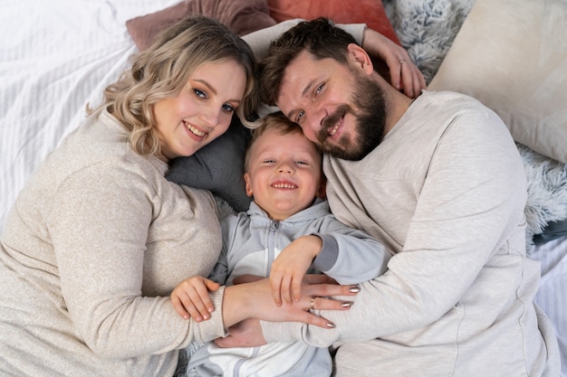 Concetto di famiglia felice Madre padre e figlio si divertono a casa Famiglia caucasica al chiuso Mamma incinta barba papà e ragazzino divertente si trovano sul divano