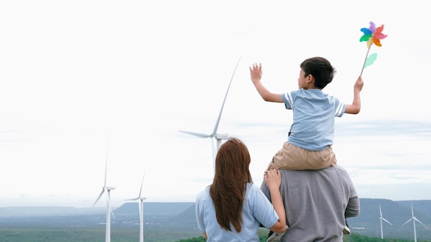 Concetto di famiglia felice progressista che si gode il tempo trascorso presso il parco eolico Generatore elettrico dal vento tramite generatore eolico in campagna con collina e montagna all'orizzonte