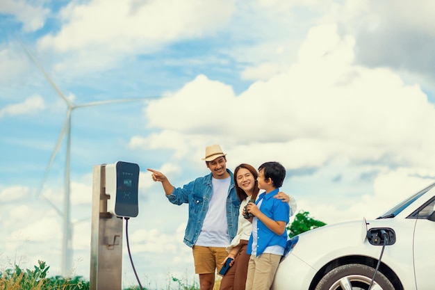 Concetto di famiglia felice progressiva al parco eolico con veicolo elettrico