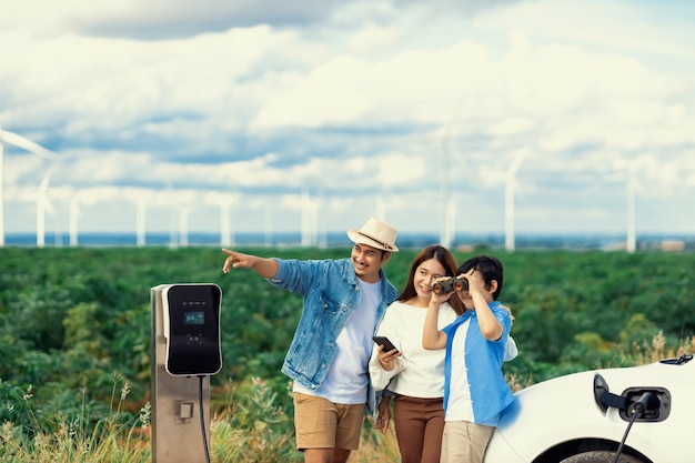 Concetto di famiglia felice progressiva al parco eolico con veicolo elettrico