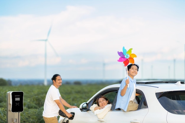 Concetto di famiglia felice progressiva al parco eolico con veicolo elettrico