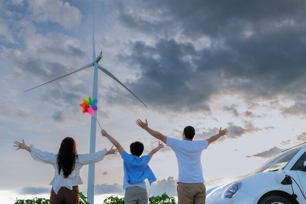 Concetto di famiglia felice progressiva al parco eolico con veicolo elettrico