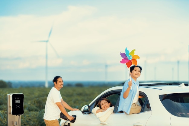 Concetto di famiglia felice progressiva al parco eolico con veicolo elettrico