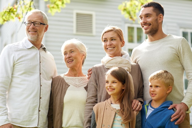 concetto di famiglia, felicità, generazione, casa e persone - famiglia felice in piedi davanti alla casa all'aperto