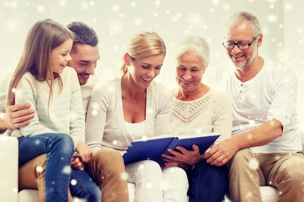 concetto di famiglia, felicità, generazione e persone - famiglia felice con libro o album fotografico seduto sul divano a casa