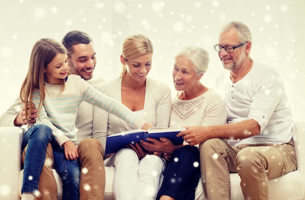 concetto di famiglia, felicità, generazione e persone - famiglia felice con libro o album fotografico seduto sul divano a casa