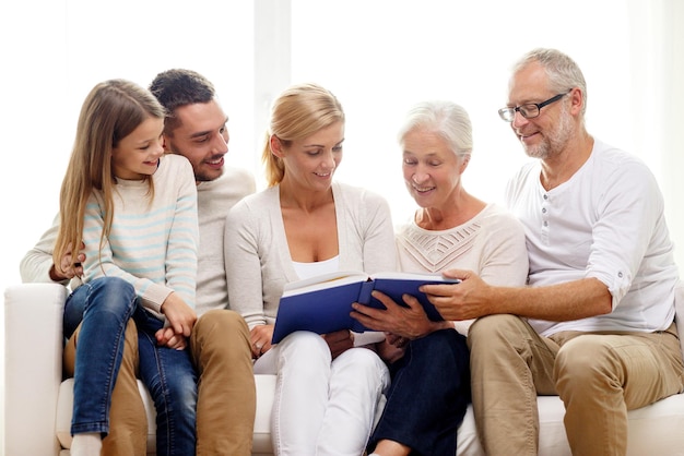 concetto di famiglia, felicità, generazione e persone - famiglia felice con libro o album fotografico seduto sul divano a casa