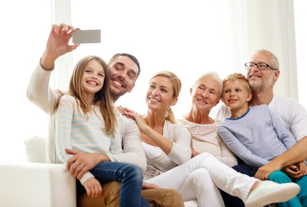 concetto di famiglia, felicità, generazione e persone - famiglia felice seduta sul divano e fare selfie con lo smartphone a casa